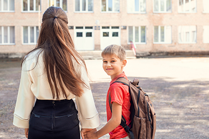 Mom and her son going to school with the son looking back at the camera