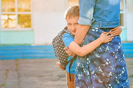 Mom and her son going to school with the son hugging his mom